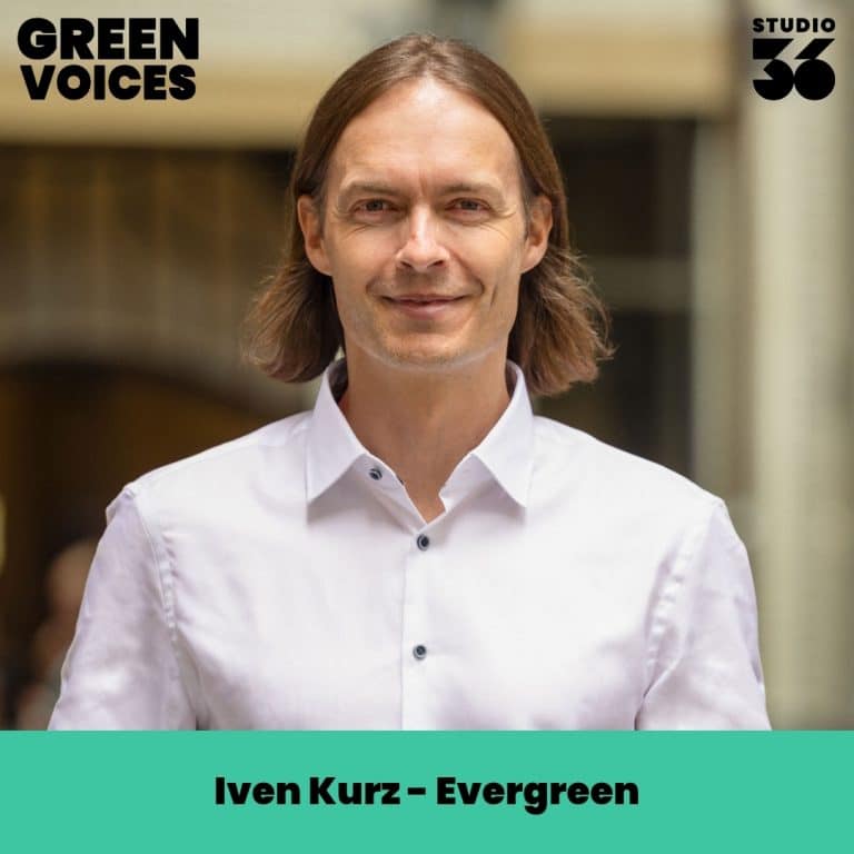 Iven Kurz mit langen Haaren in einem weißen Hemd, lächelt vor einem unscharfen Hintergrund.